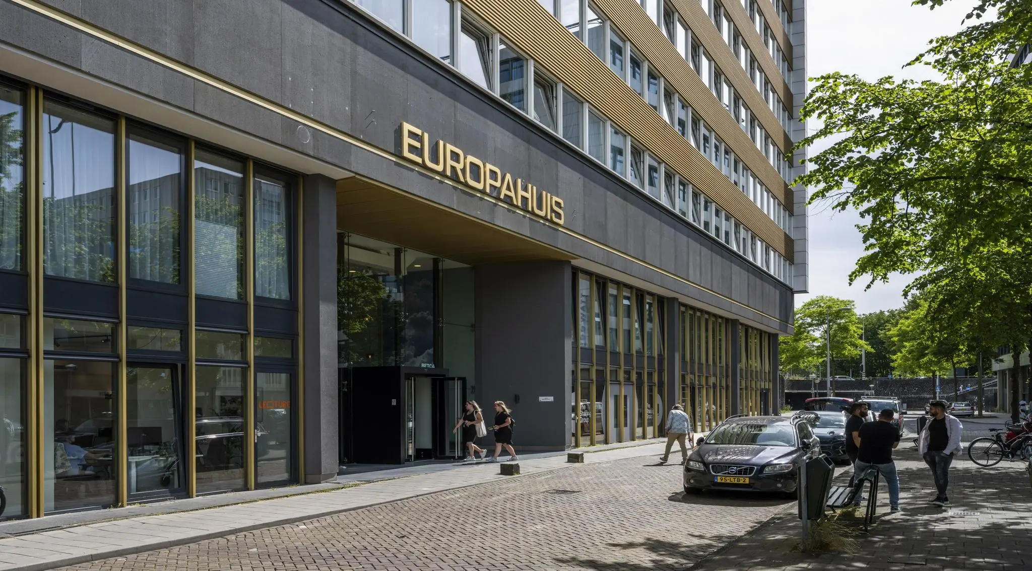 Voorgevel van het Europahuis aan de James Wattstraat met mensen bij de ingang en geparkeerde auto's langs de straat.